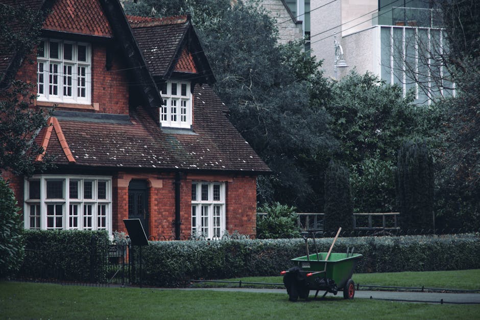 A landscaped park area featuring a circular gazebo with a metal roof supported by decorative columns, surrounded by a low brick wall with a green wooden railing. The foreground shows a curved brick fl